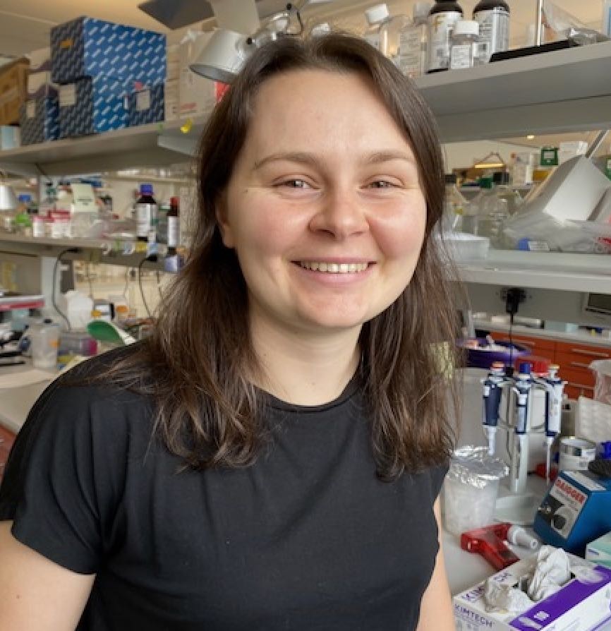 Grad student Isabella is smiling in front of her bench.