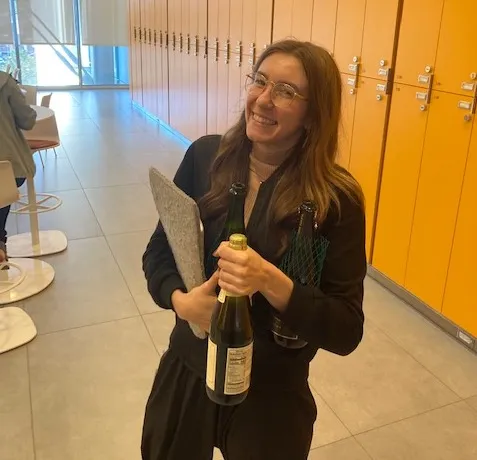 Alexa is smiling while carrying her laptop sleeve as well as opened and an unopened bottle. 