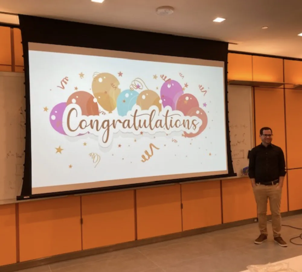 Hani is standing next to a large sign with balloons that says "Congratulations"
