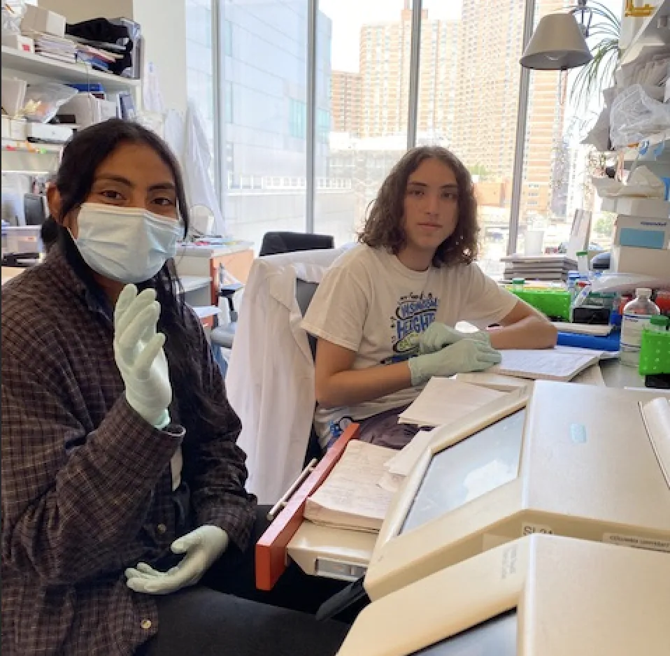 America is in front of the PCR machine and Aldo is writing in his notebook next to her. 