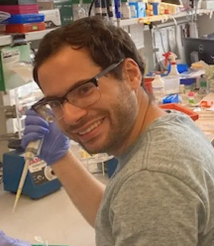 Hani Shayya is holding a pipettor while wearing a purple glove and working with tubes on his bench.